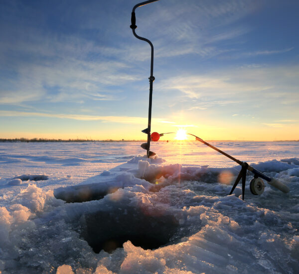 close-up drill, fishing rod near the hole on the ice in winter river at sunset