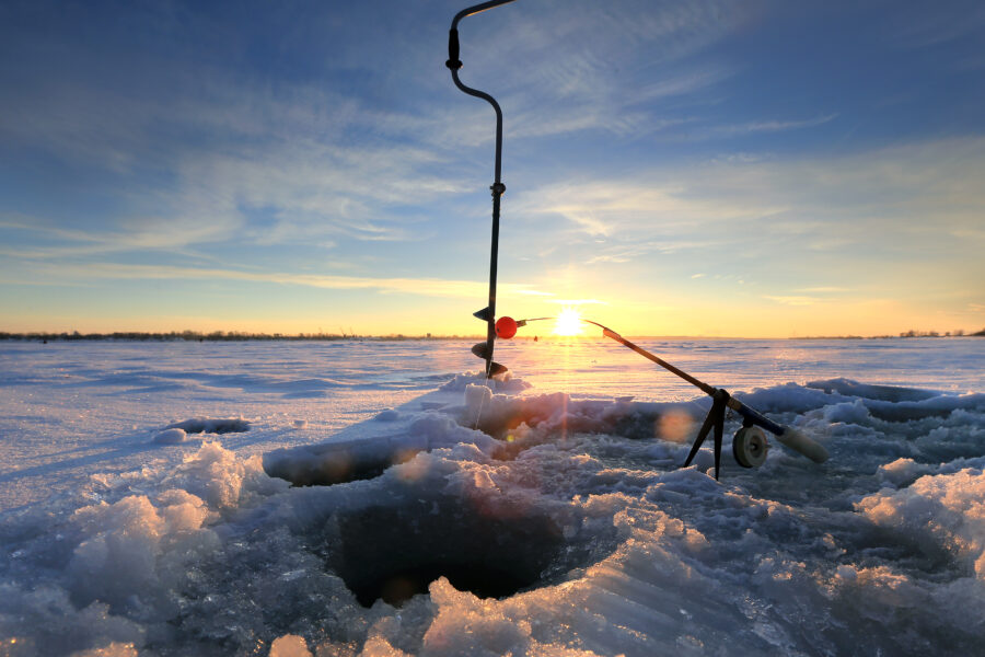 close-up drill, fishing rod near the hole on the ice in winter river at sunset